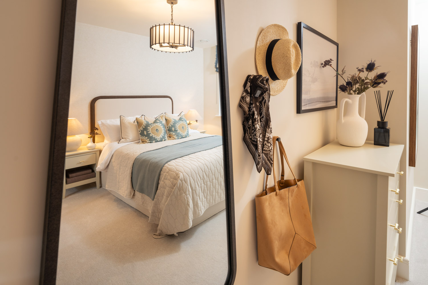 Reflection of made up blue and cream bed in a full length mirror propped against the wall, hat bag and scarf in the background